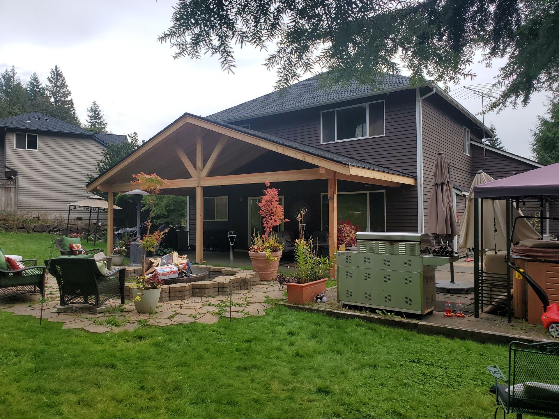 Backyard with a brown house, covered patio, fire pit, and green lawn.