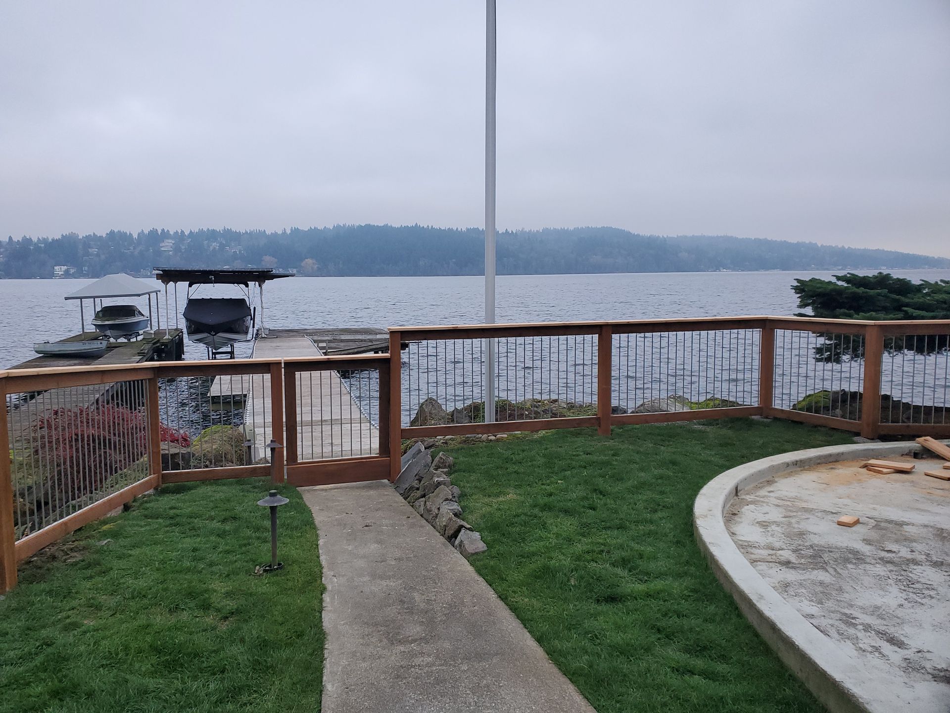 A wooden fence and gate lead to a lake with a boat dock on an overcast day.