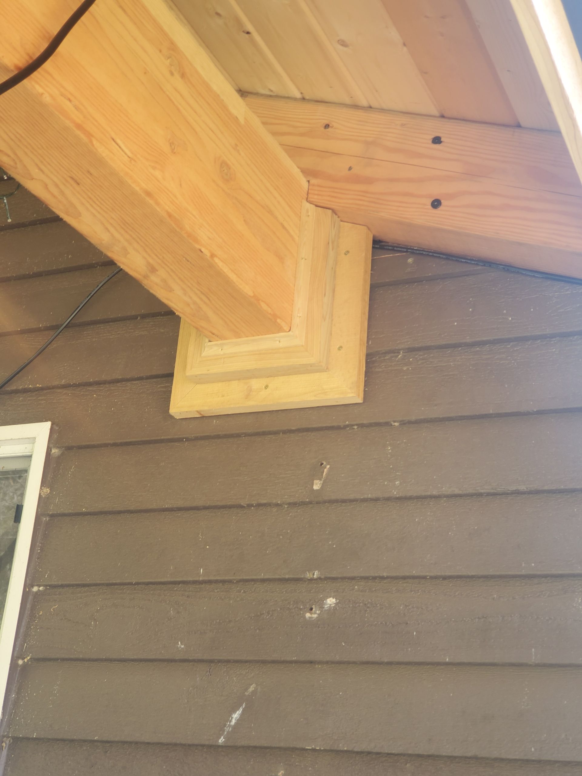 Wooden beam supported by decorative bracket on a brown house exterior.