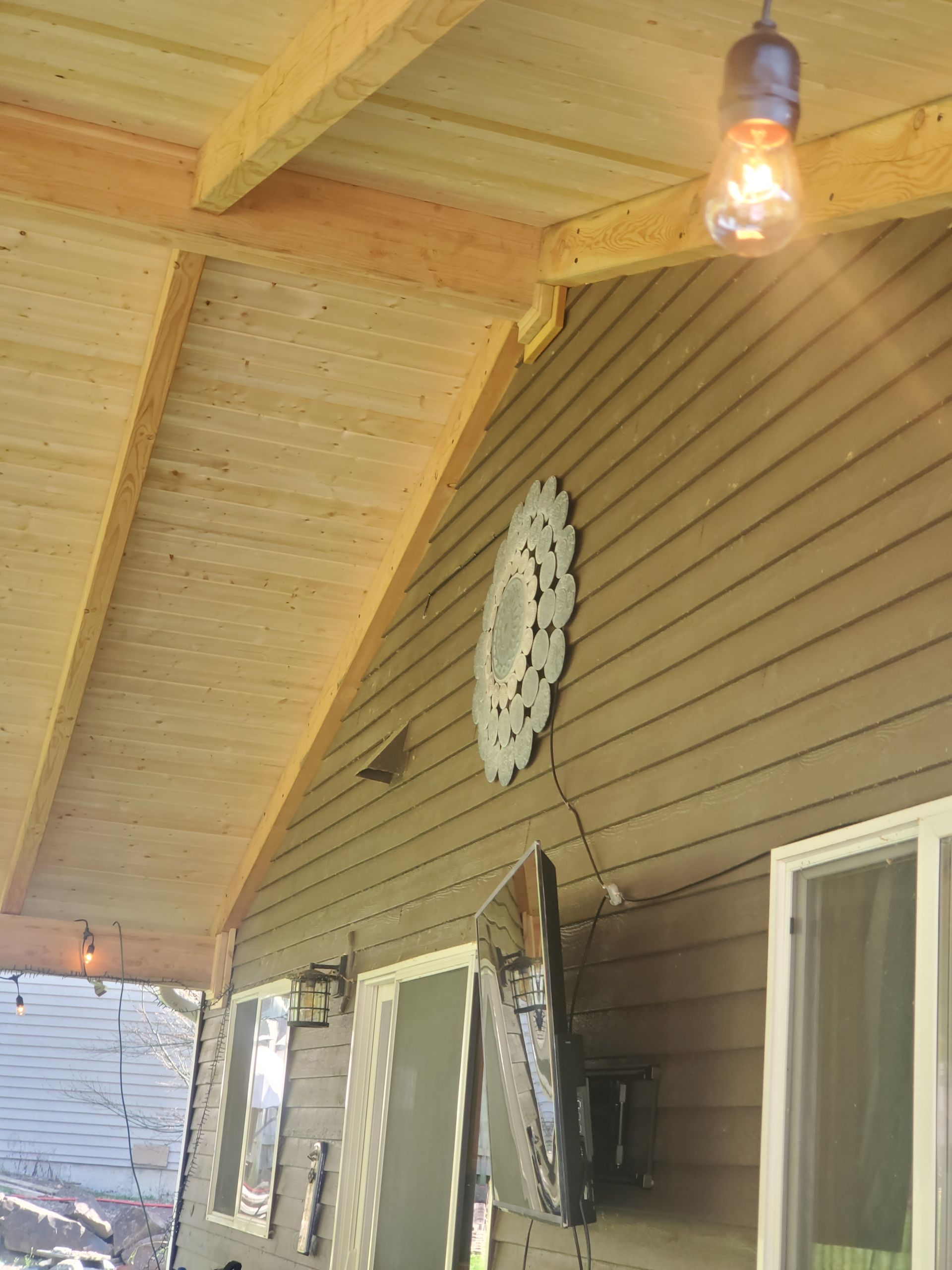 Covered porch with light bulb, decorative wall art, and siding.