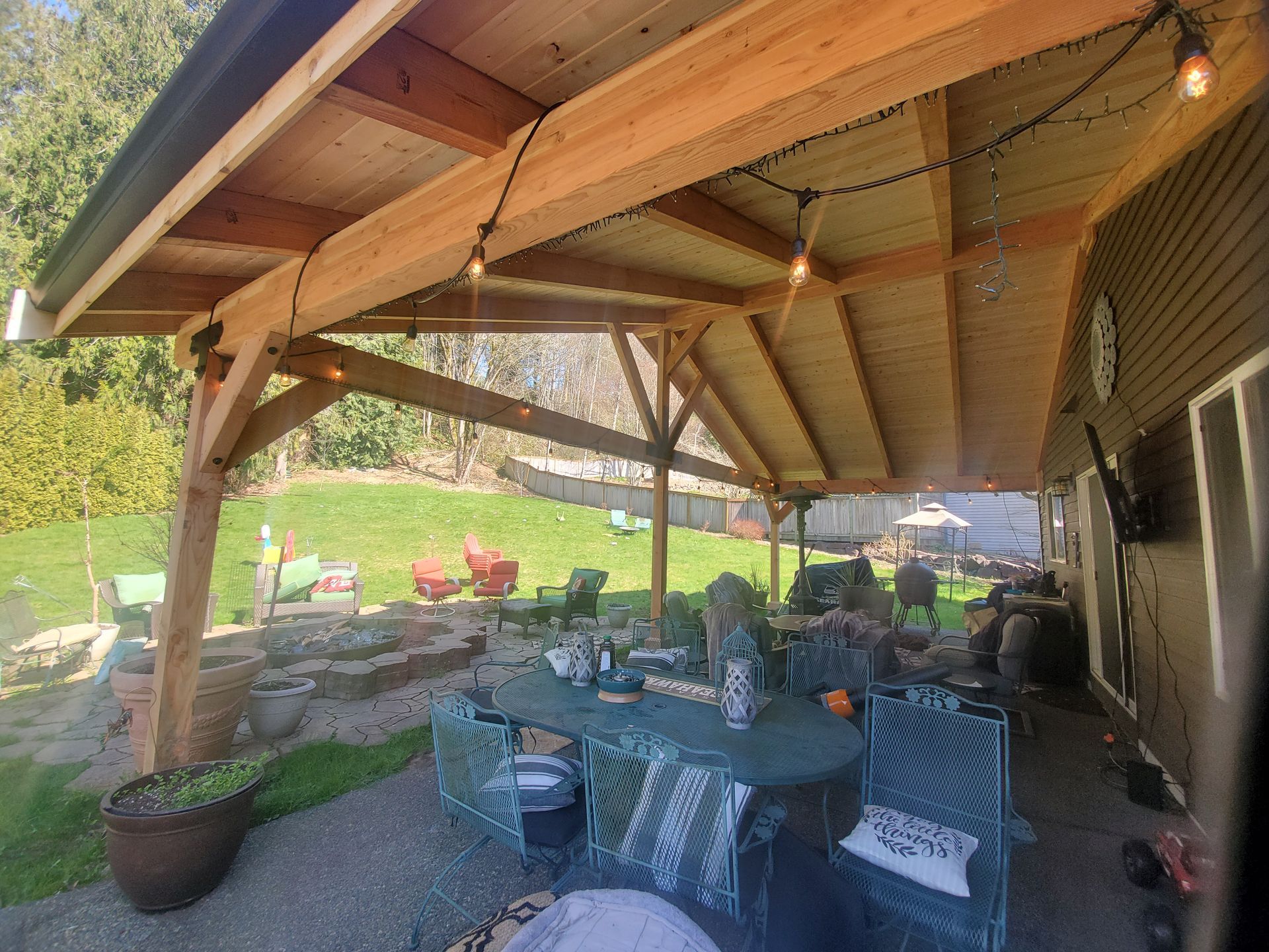 Wooden patio cover over outdoor dining area with string lights and garden in the background.