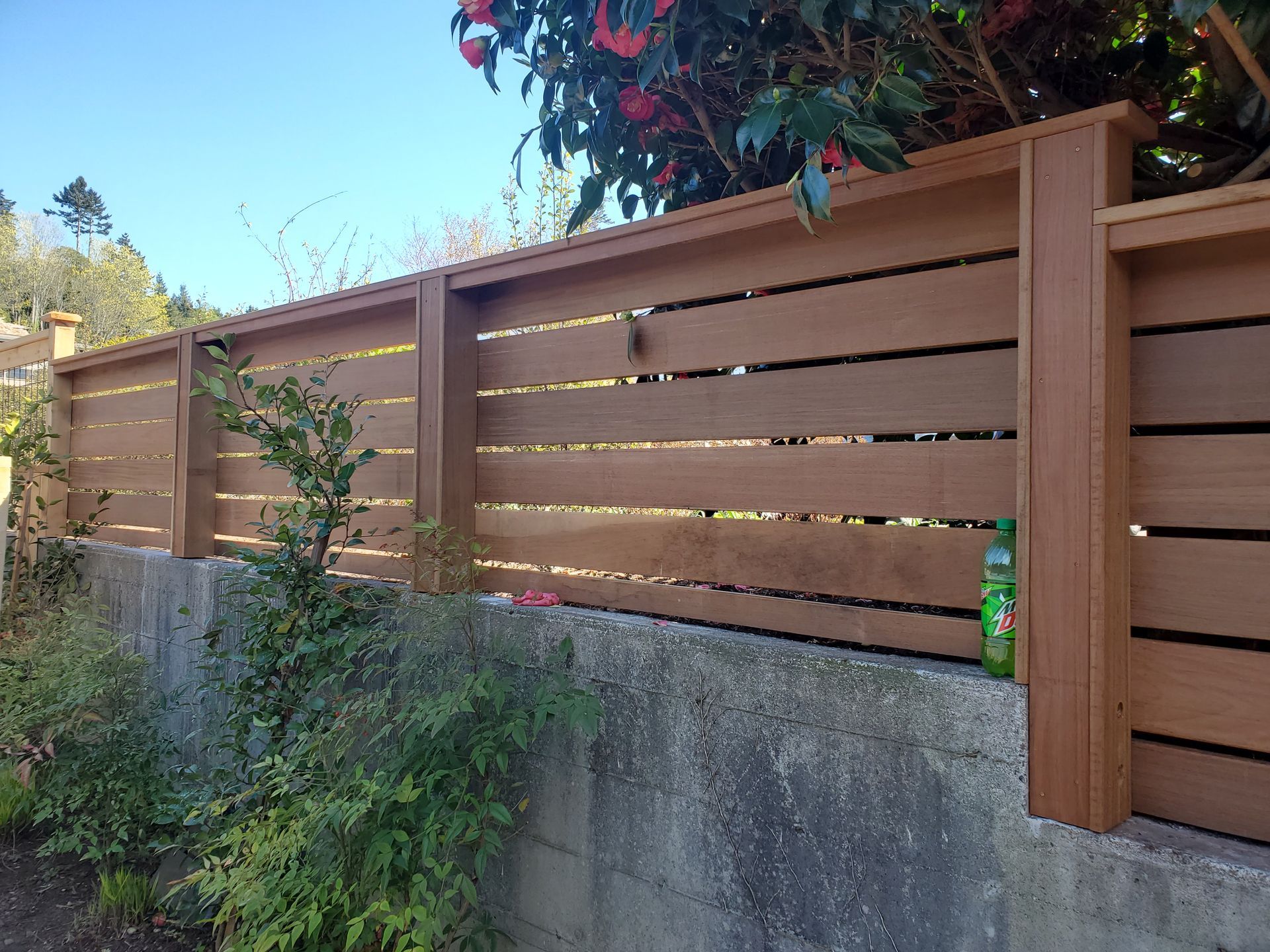 Wooden horizontal slat fence atop a concrete wall, with green foliage.