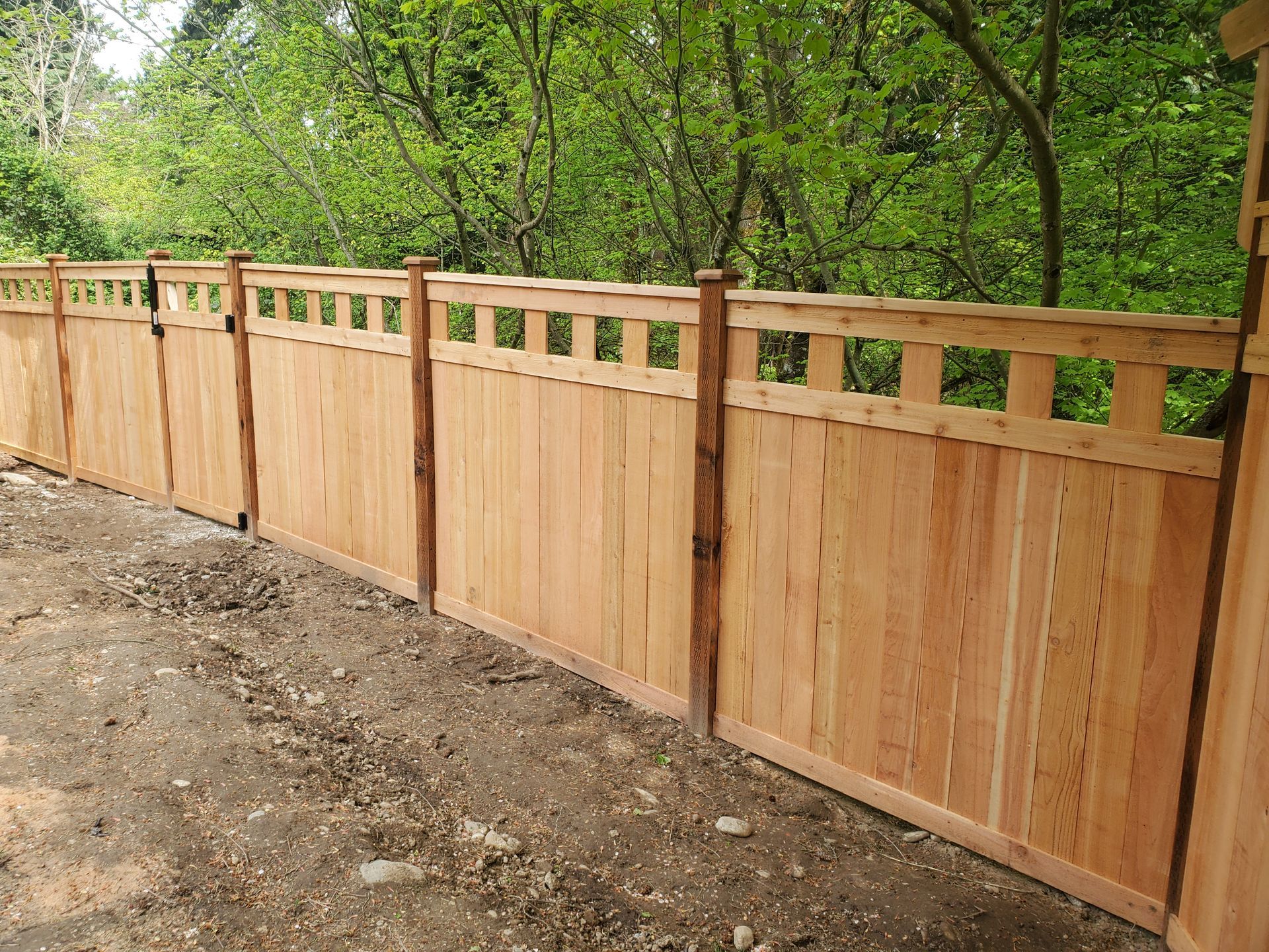 Wooden fence with decorative top, in front of trees.