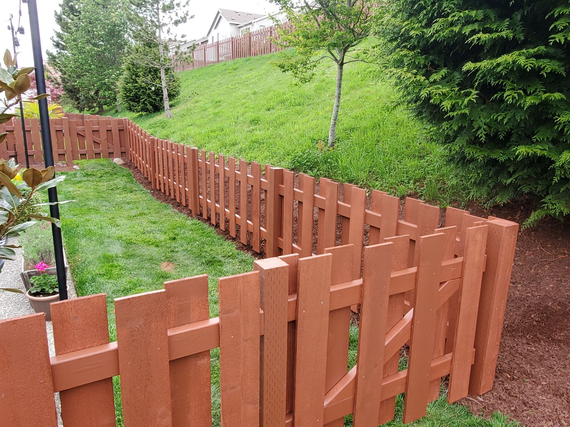 Brown picket fence enclosing a grassy yard on a slight hill.