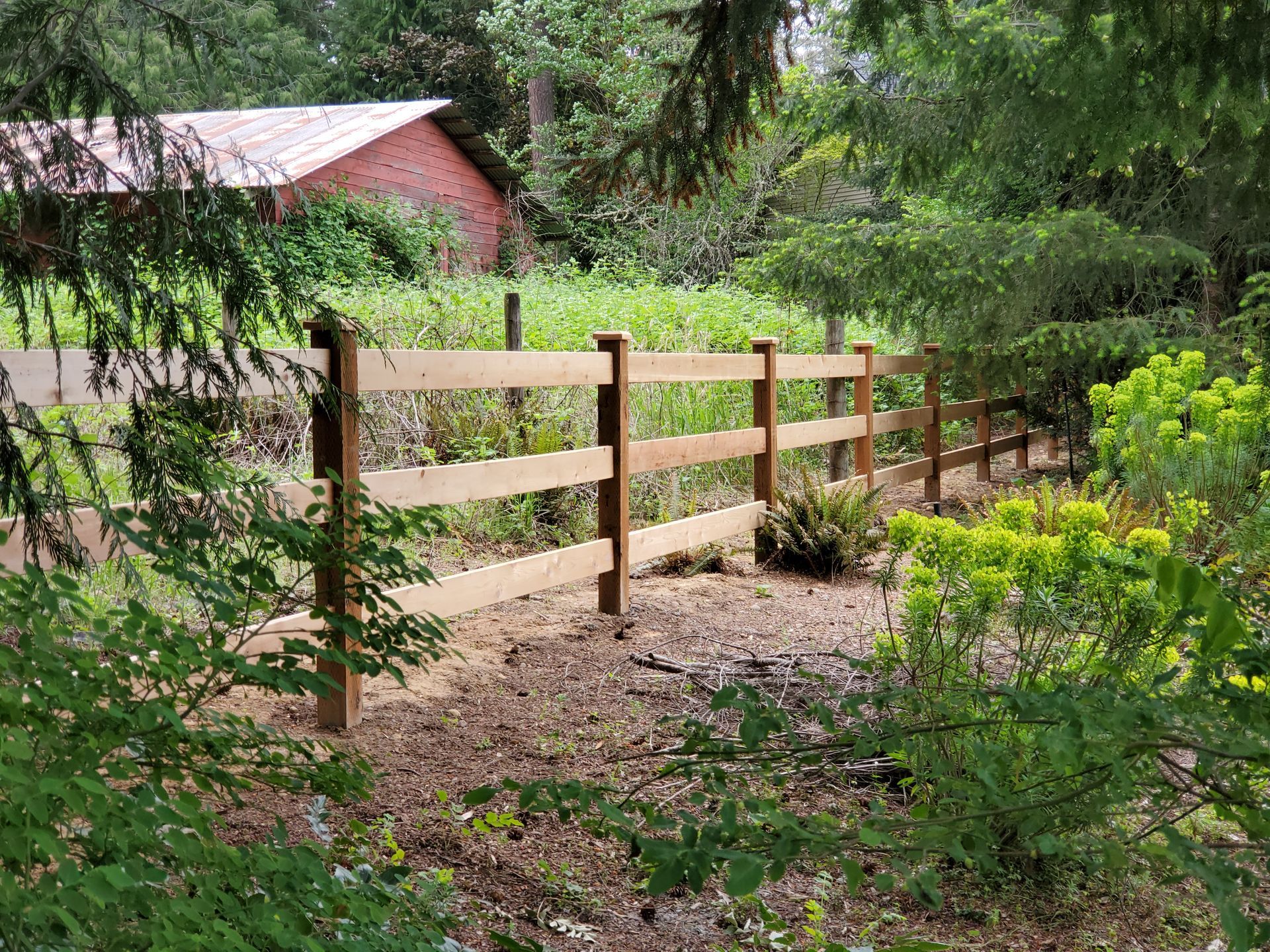 Wooden fence in a natural setting, with a red barn in the background.