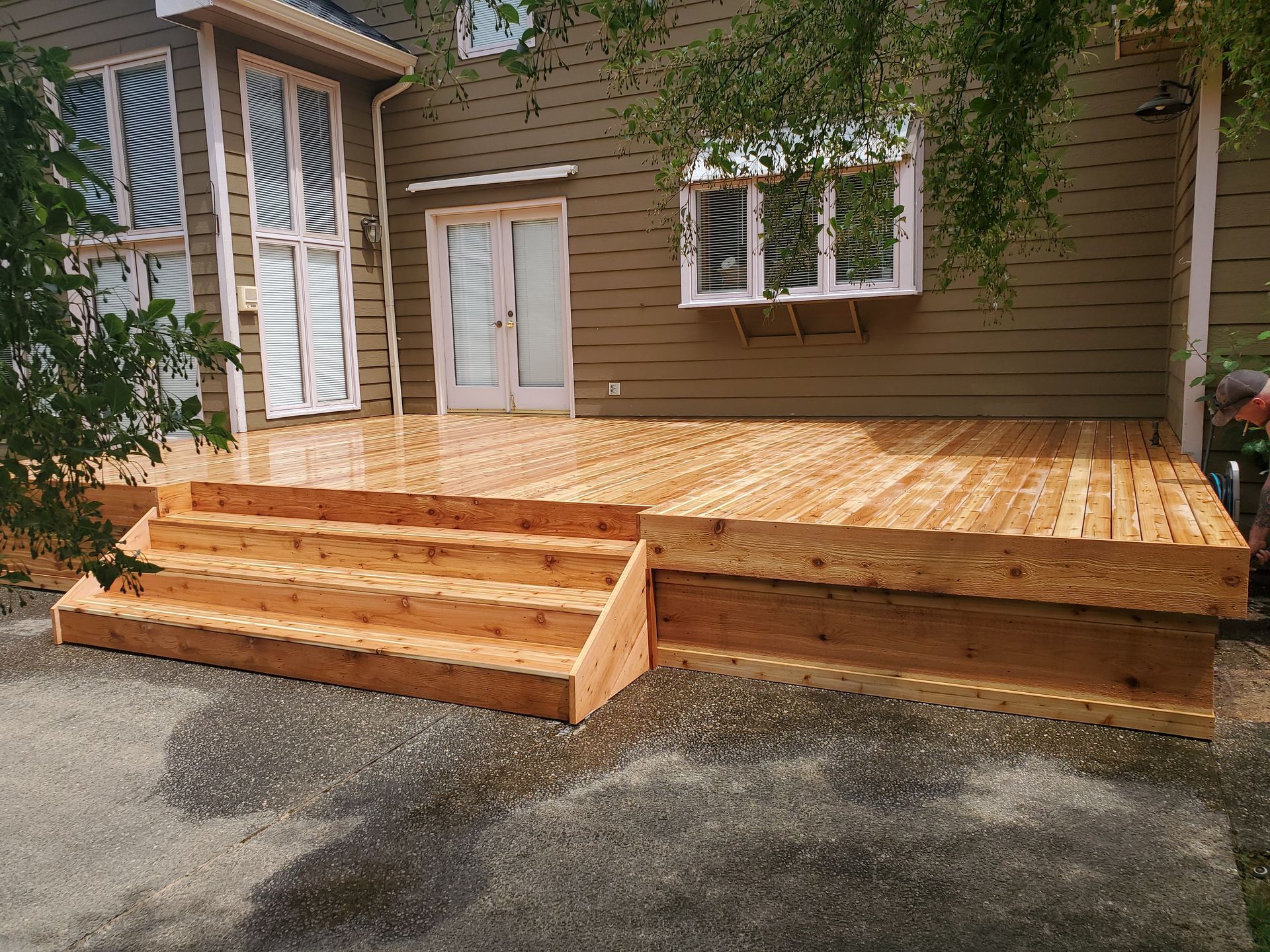 Newly constructed wooden deck with steps attached to a brown house with white trim.