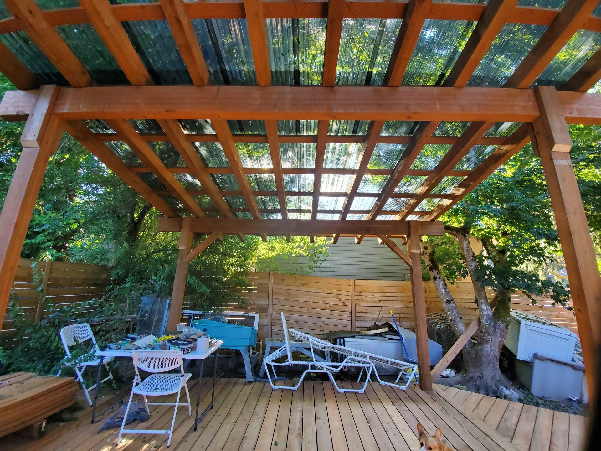 Wooden pergola over a deck, with chairs and table, backyard setting.