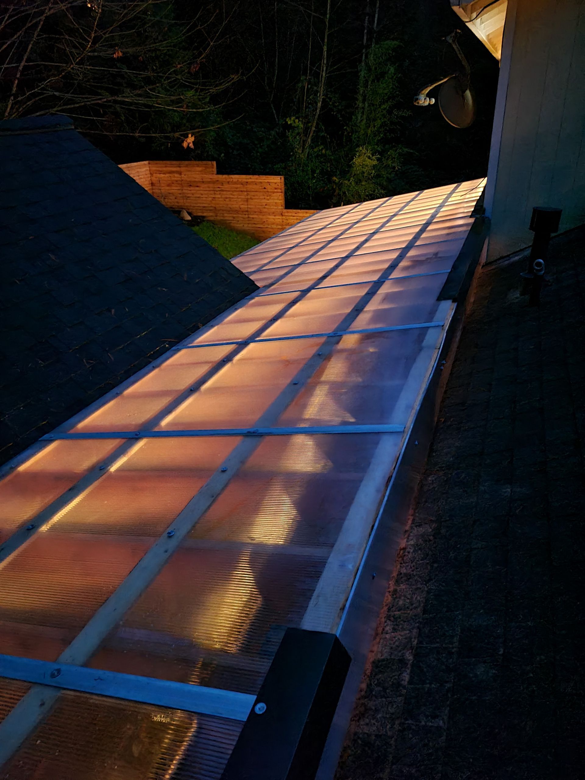 Translucent roof panels on a metal frame, lit from below, leading toward a building.