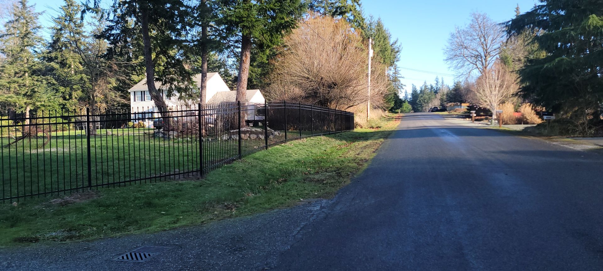 A paved road winds through a neighborhood, with a house behind a black fence on one side.