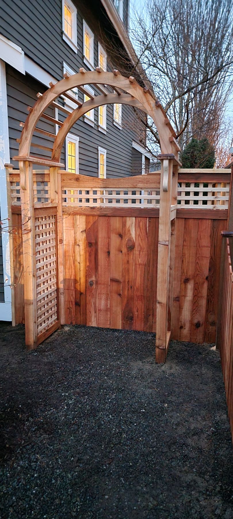 Wooden arbor and privacy fence in an outdoor space, with dark gravel ground.