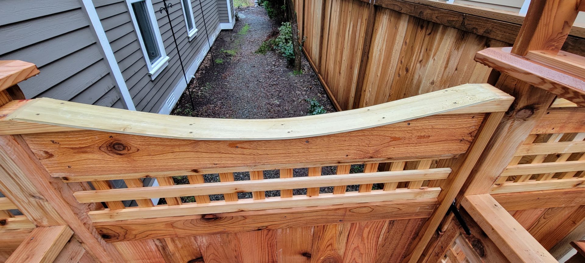 Wooden fence with decorative lattice detail, framing a narrow walkway between buildings.