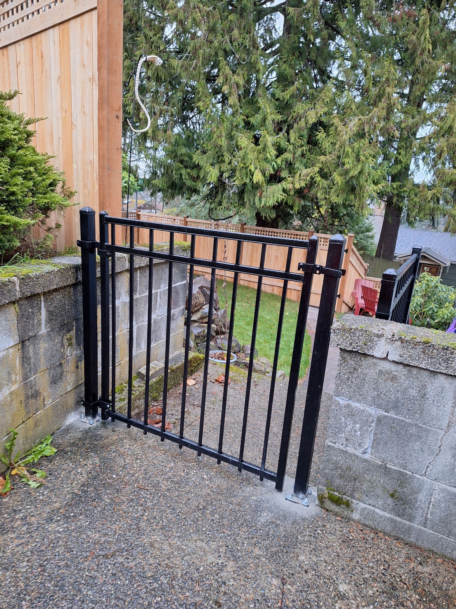 Black metal gate in a concrete wall, leading to a grassy area with trees in the background.