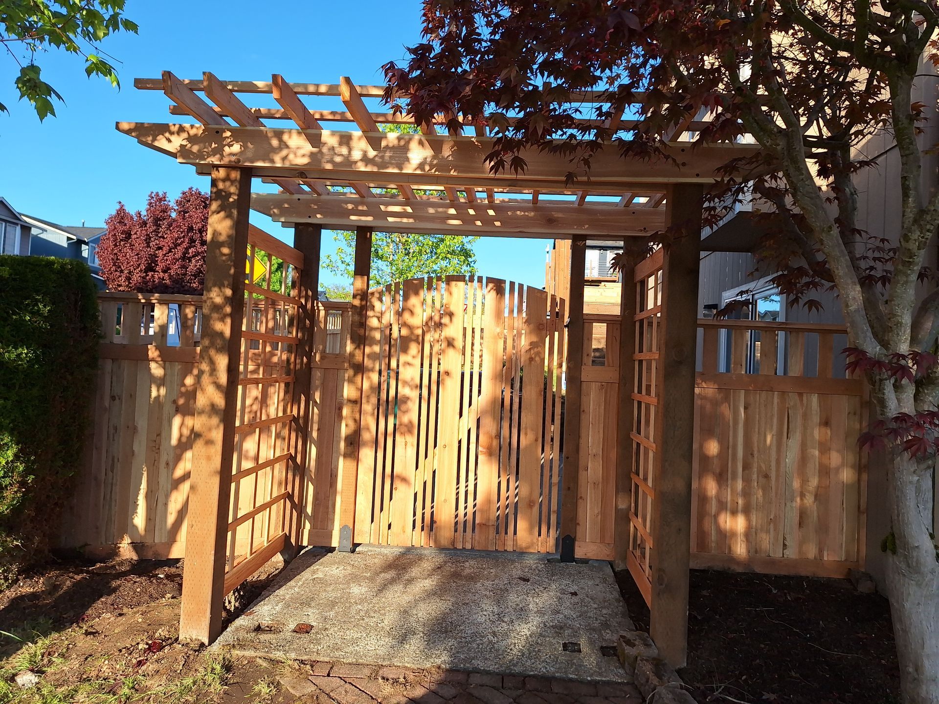 Wooden pergola gate in a backyard, leading to a fenced area.