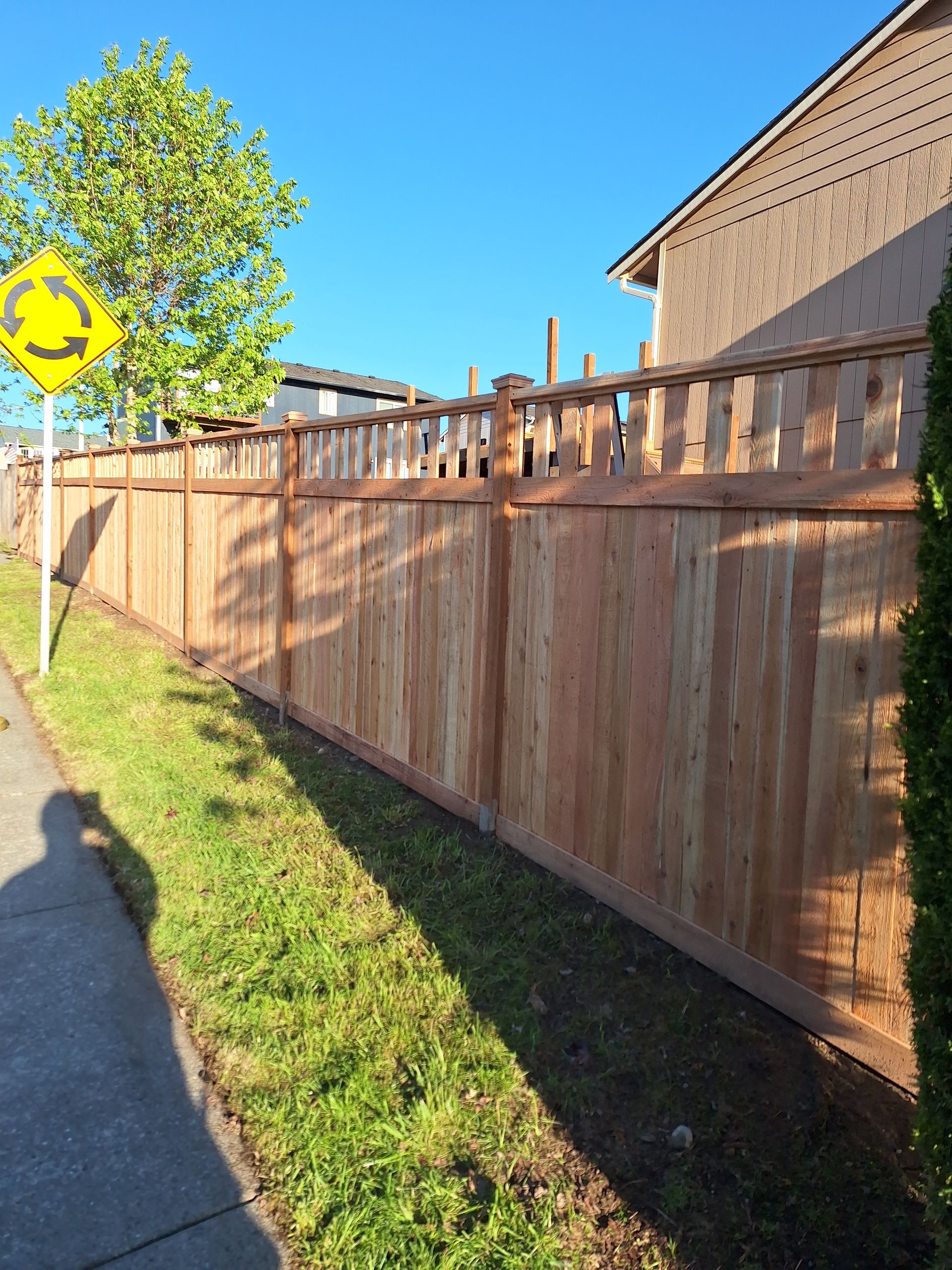 Wooden fence along a sidewalk, with a traffic sign and a house visible.