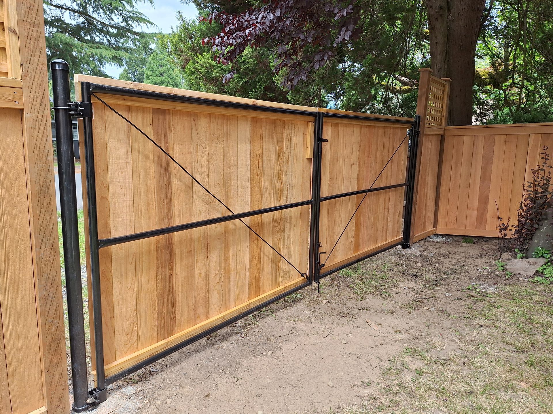 Wooden fence gate with black metal frame and diagonal supports, set in a yard.