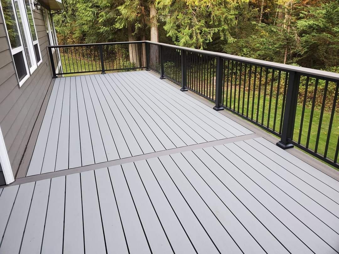 Gray composite deck with black railing overlooking a green yard and trees.