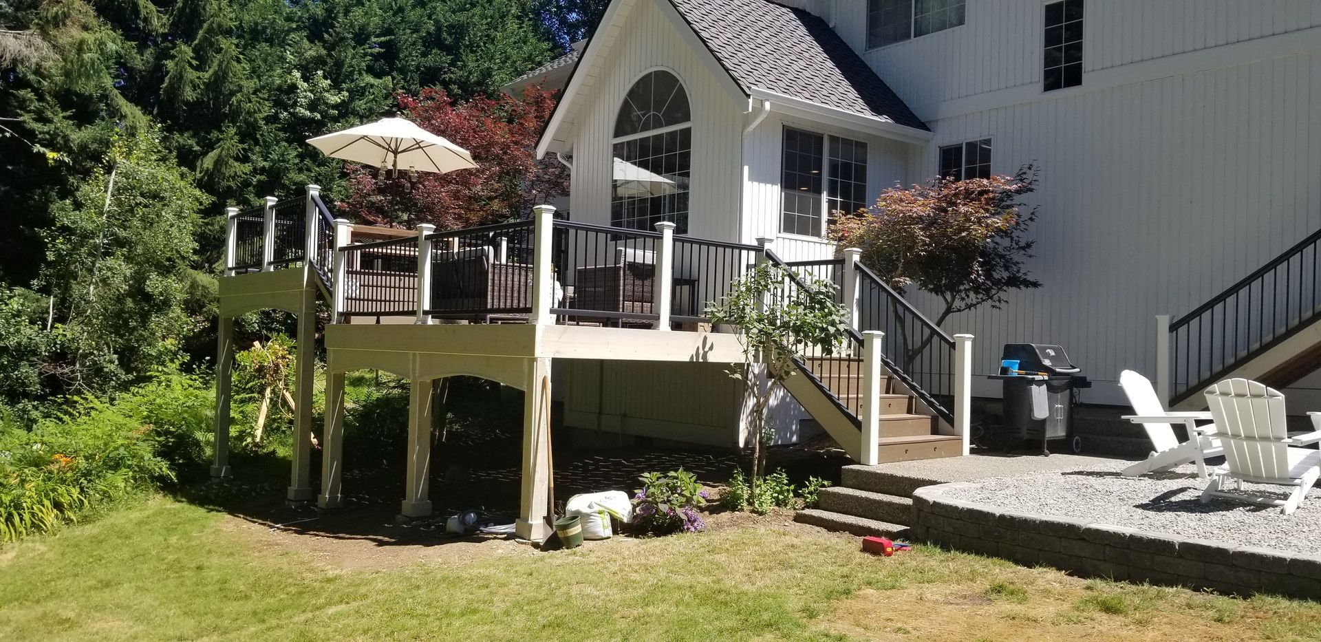 Backyard deck with furniture and umbrella, adjacent to a white house with a black staircase.