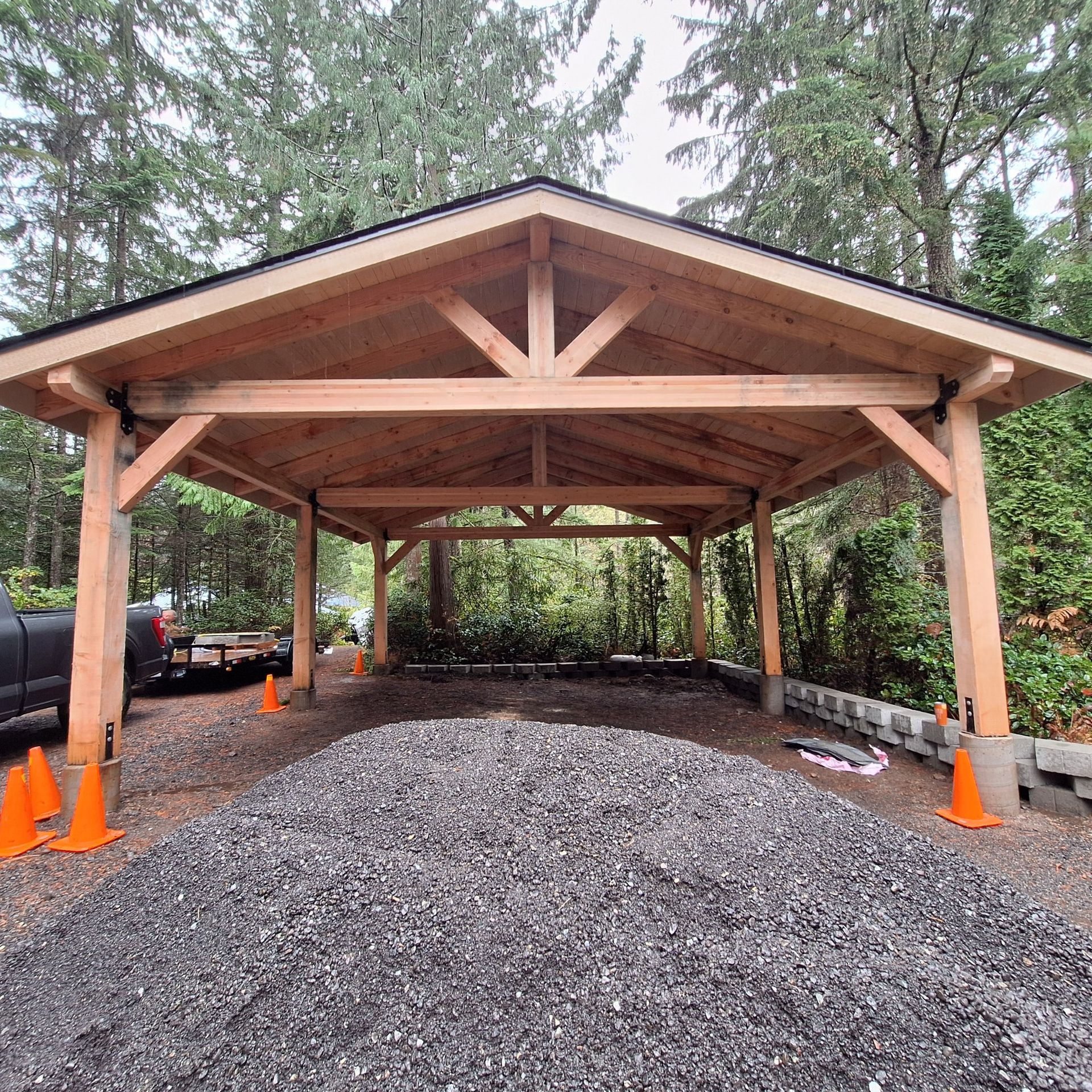 Wooden carport with gravel driveway and orange traffic cones.
