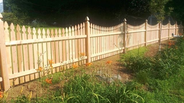 Wooden picket fence along a grassy area, with orange flowers in the foreground.