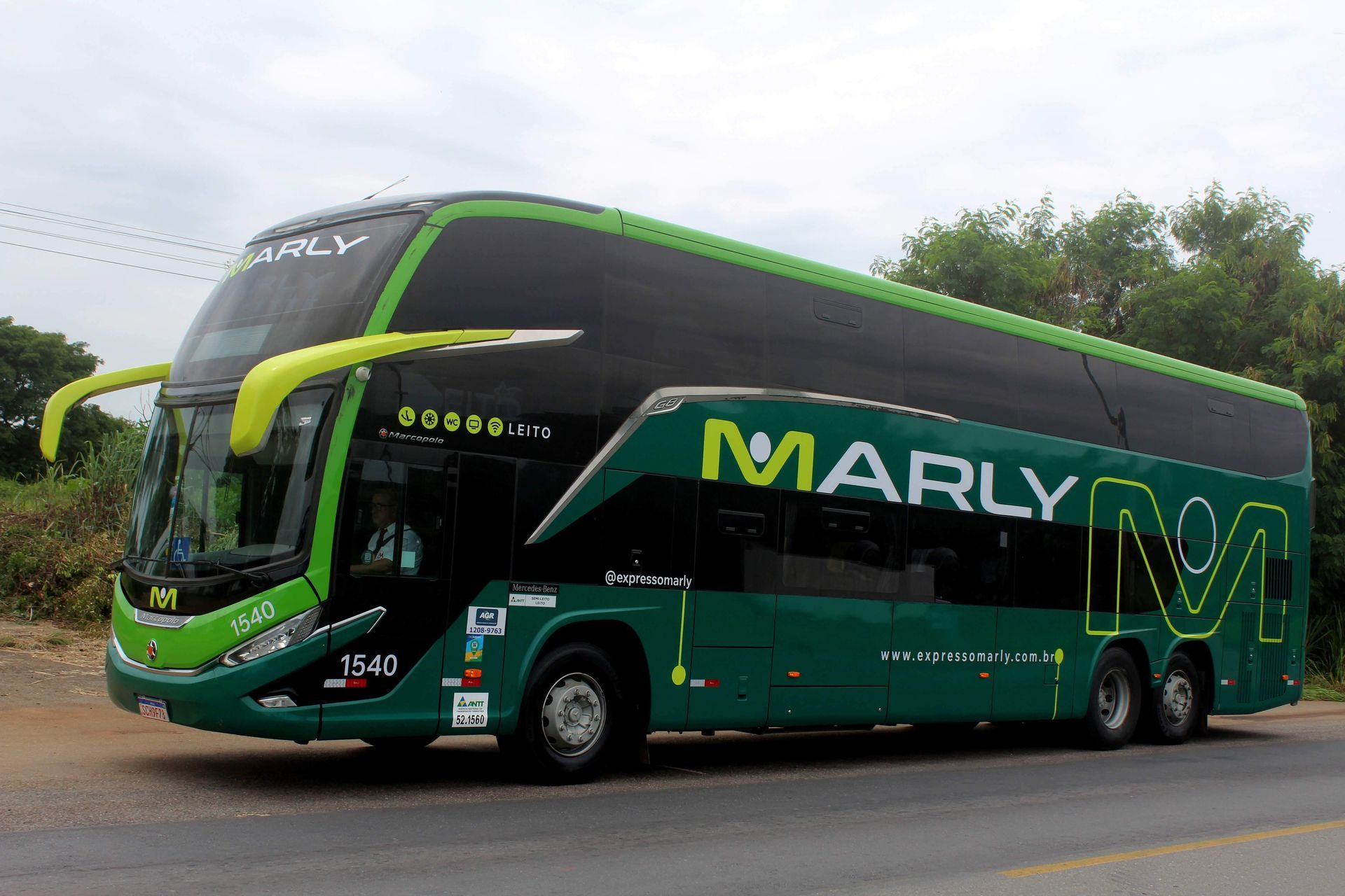 Ônibus verde de dois andares, da marca "Marly", estacionado em uma estrada.