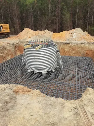 A corrugated steel form sits in a dirt excavation on top of a steel rebar grid for a wind turbine foundation.