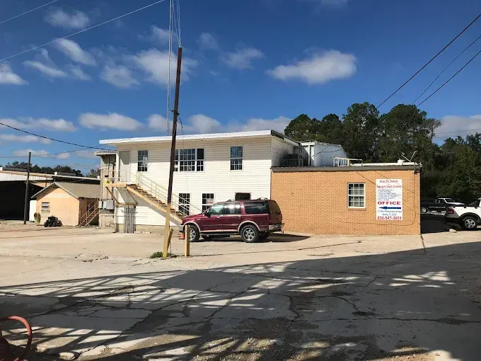 A two-story white building with an external staircase and a tan brick extension under a clear blue sky.