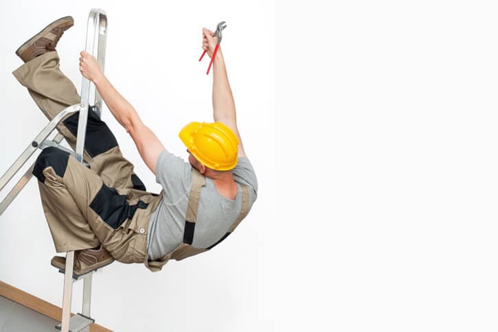 A worker in a yellow hard hat falls from a ladder, holding pliers, against a white wall.