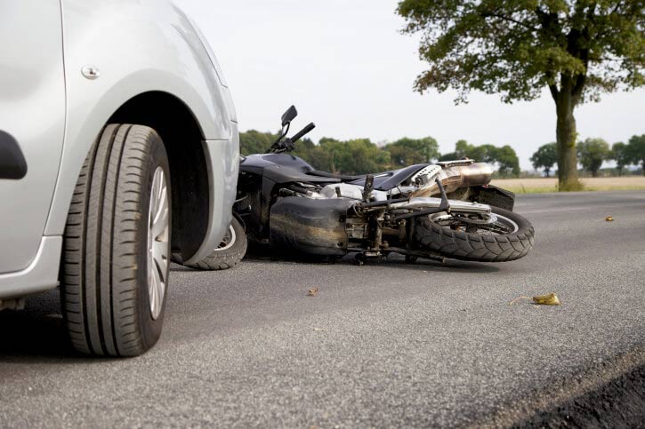 A silver car and a motorcycle lie on their sides on a road after a collision.