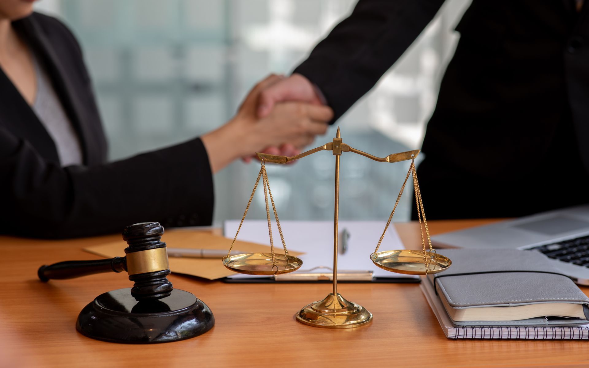 Legal consultation handshake with scales of justice, gavel and documents on office desk setting area.