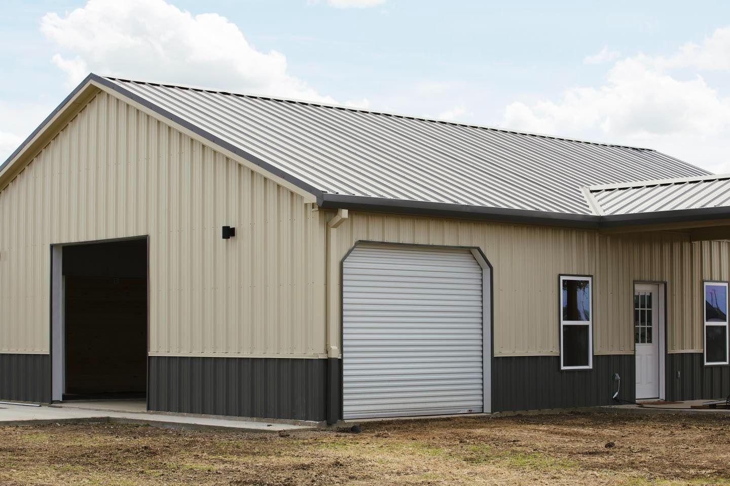 A large metal building with a garage door is sitting in the middle of a field.