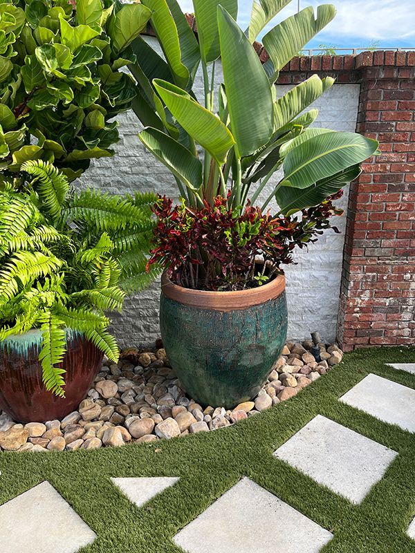 rocks and large pots along fence with square concrete stones inside artificial grass