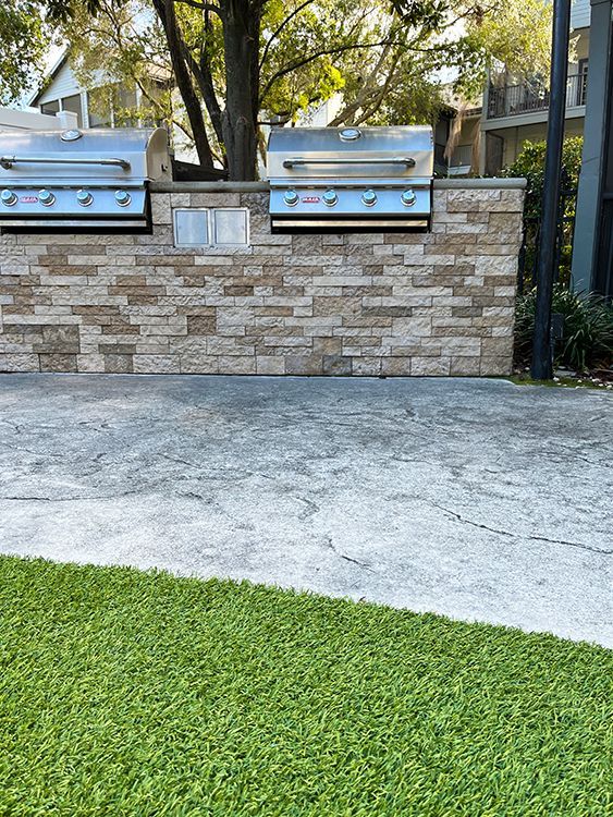 Outdoor dual grill setup surrounded by artificial turf in the pool area of a Hyde Park apartment complex