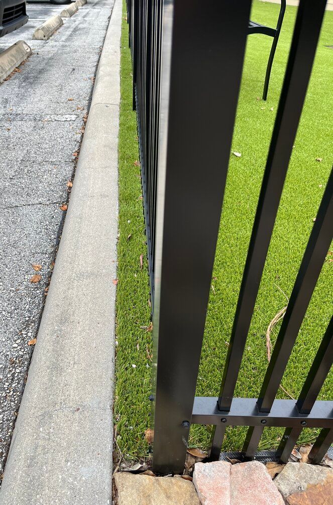 parking lot curb with nice turf edge along a black aluminum fence at a dog run