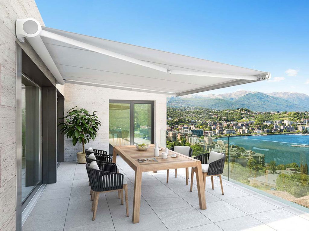 Un balcone con tavolo e sedie sotto una tenda da sole con vista sul lago.