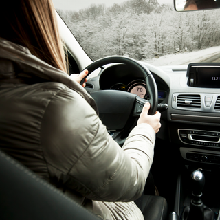 A woman is driving a car with a clock on the dashboard that says 12:51