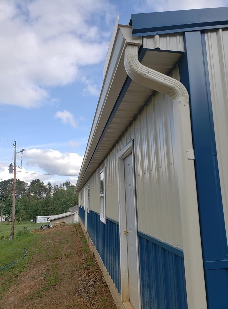 Hands use a power drill to fasten a metal gutter section to the corner of a house exterior.