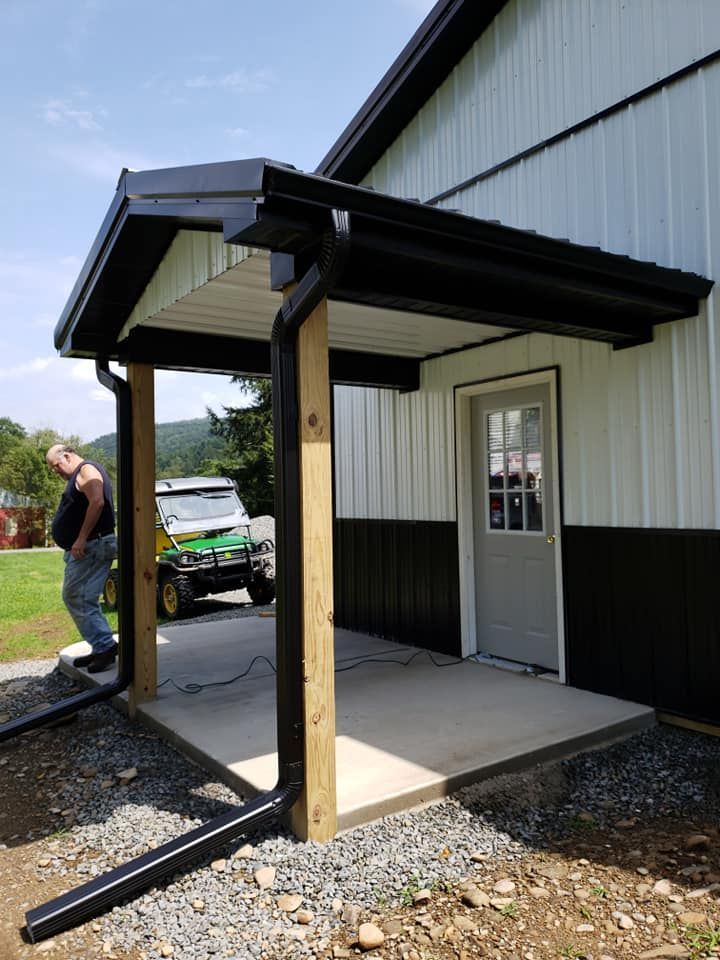 A beige stucco building wall with three vertical metal downspouts over a brown brick base against a blue sky.