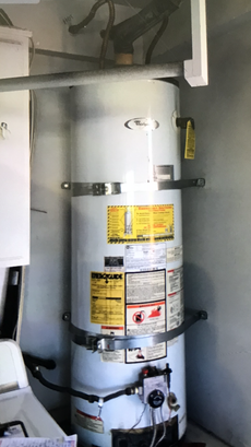 A water heater is sitting in a laundry room next to a washer and dryer.