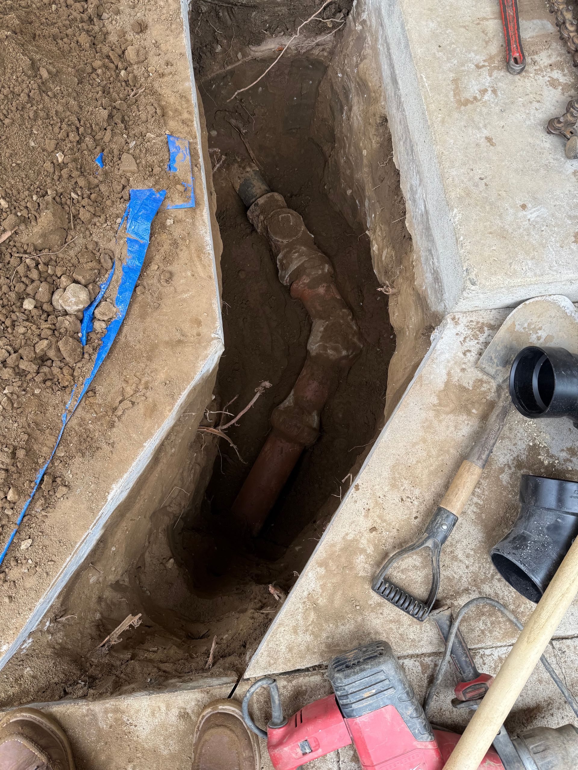 A hole in the ground with a pipe in it and tools on the ground.