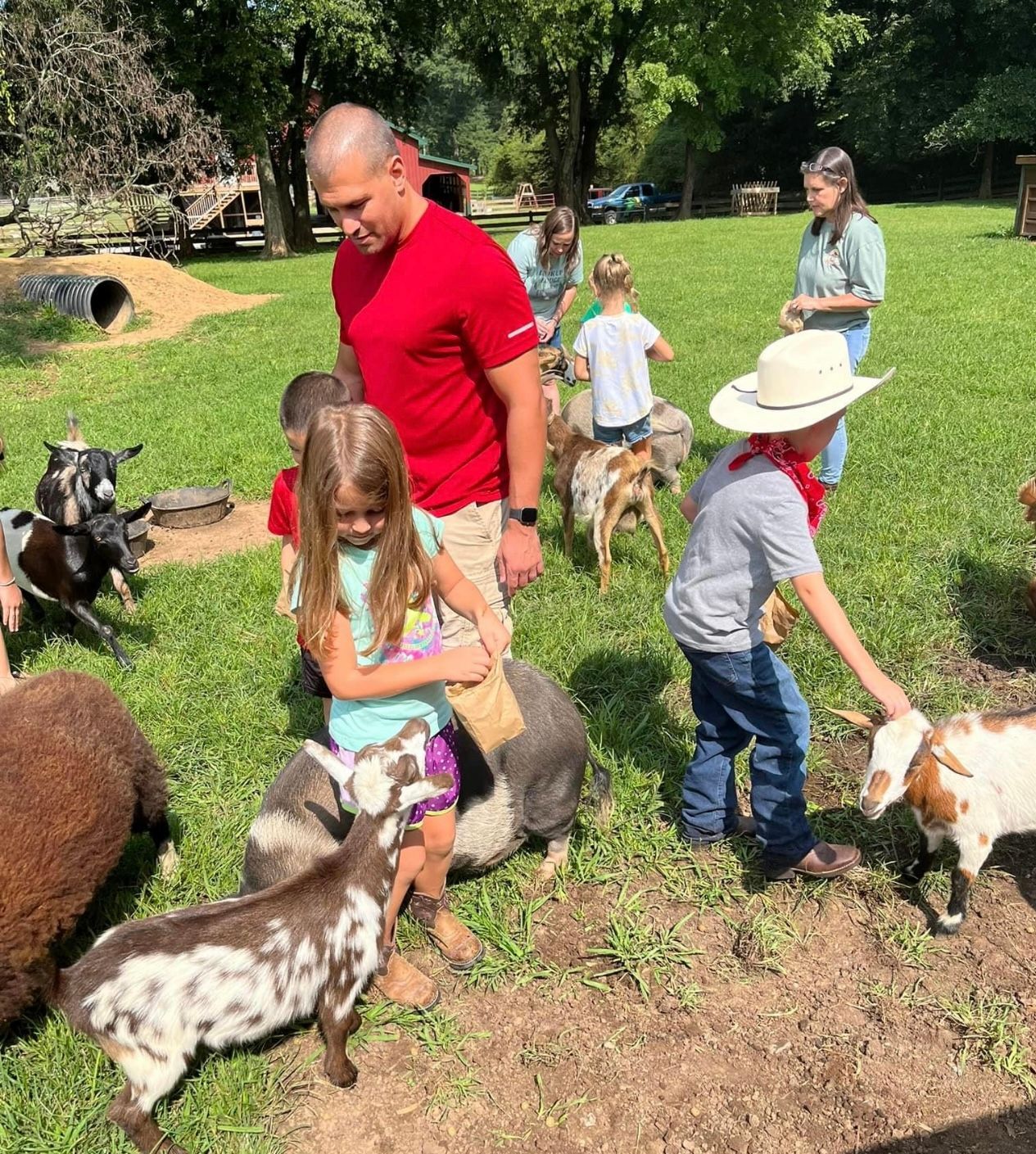 A group of people are standing in a grassy field with goats.