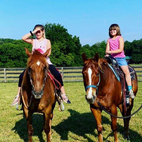 Two young girls are riding horses in a grassy field