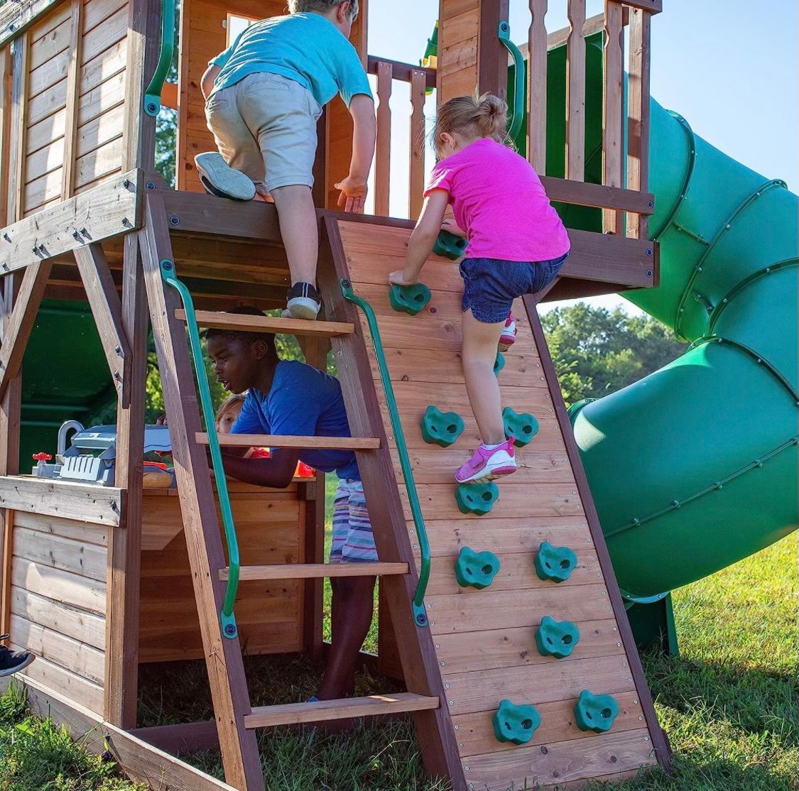 A boy and a girl are playing on a wooden playground with a green slide