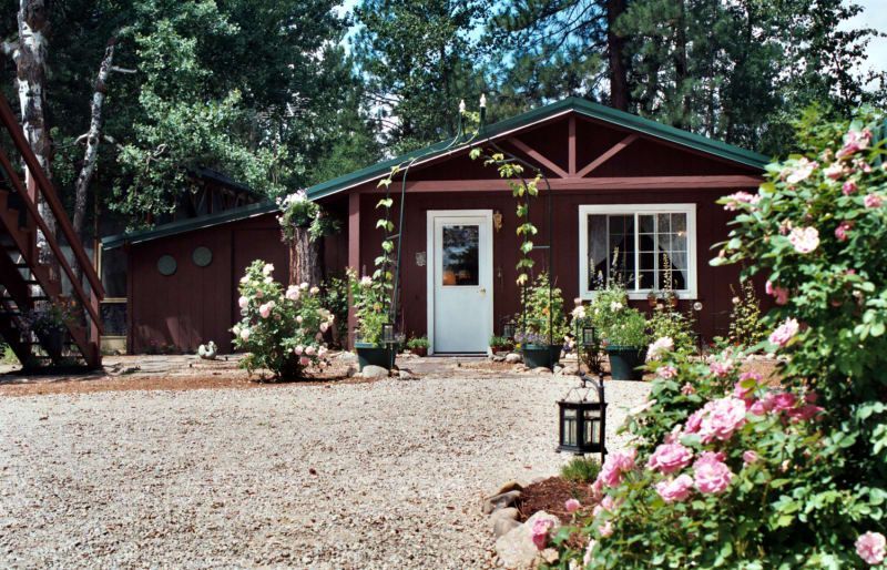 A red house with a white door is surrounded by flowers and trees.