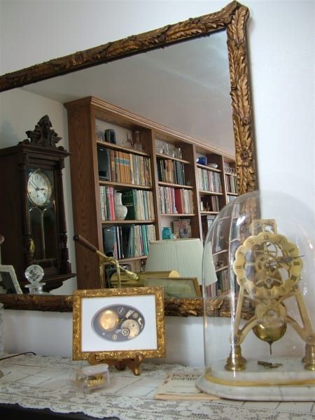 A clock in a glass dome sits on a table in front of a mirror
