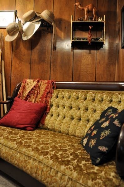 A couch with a red pillow sits in a room with wood paneling