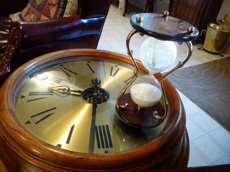 A clock with roman numerals and a hourglass on top of it