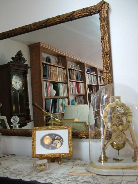 A clock in a glass dome sits in front of a large mirror