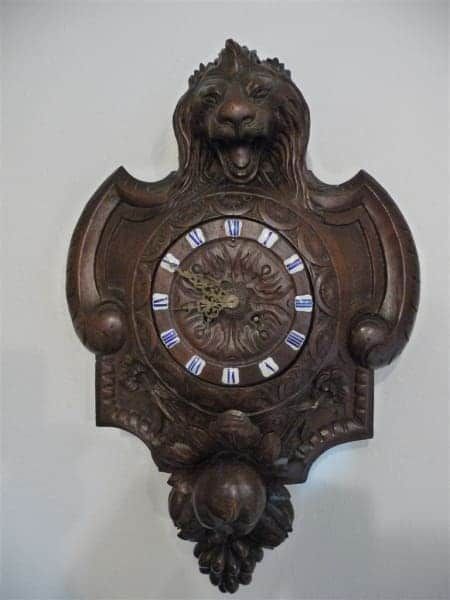 A wooden clock with roman numerals and a lion face