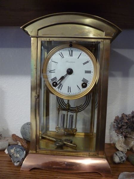A brass clock with roman numerals is on a wooden table