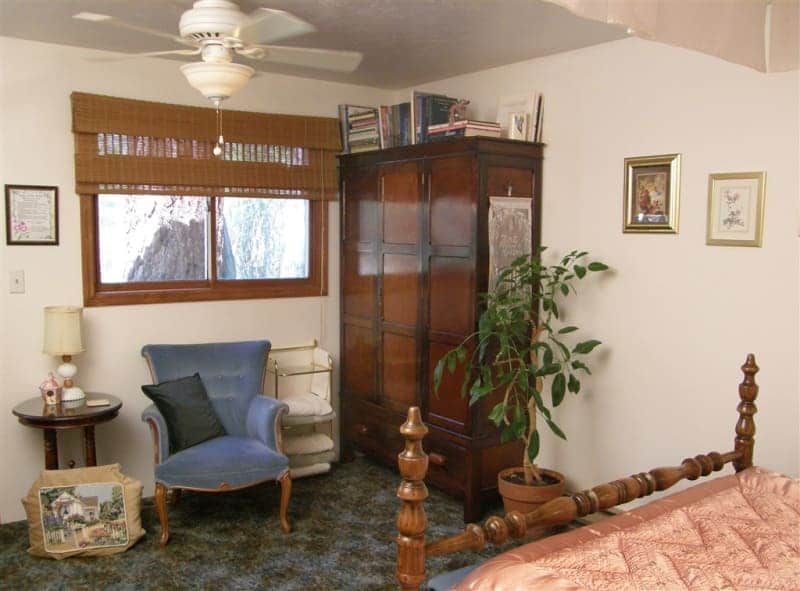 A bedroom with a bed a chair and a ceiling fan